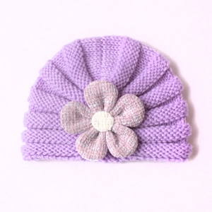 Detail of baby knitted hat featuring a lavender wave pattern and a large floral accent