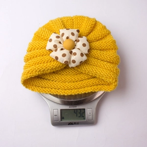 Detail view of yellow knitted baby turban hat with polka dot flower on a scale weighing 43.2g