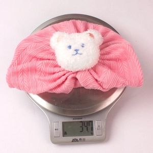 Detailansicht der rosa Baby-Strickmütze mit Plüschbär auf einer digitalen Waage