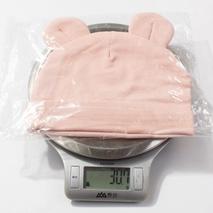 Mesure du poids d'un bonnet en modal rose pour bébé avec oreilles d'ours sur balance