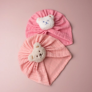 Detailansicht der Baby-Turbanmützen mit Fischgrätmuster und Plüschbären-Stickerei
