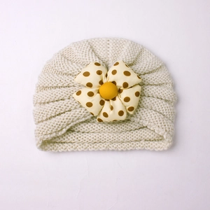 Detailed view of cream rib-knit baby hat featuring a large polka dot flower decoration