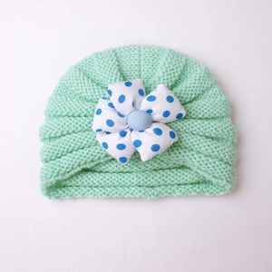Detailed knit texture of mint green baby hat featuring a white polka dot flower detail