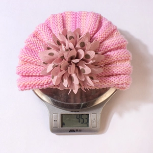 Détail montrant le bonnet en tricot rayé pour bébé pesant 45,3g sur une balance de précision