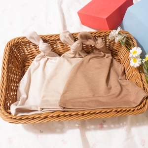 Close-up of three earth-tone newborn baby knotted beanies in a woven basket