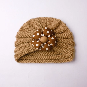 Close-up of baby knit hat showing latte thick yarn and brown polka dot fabric flower