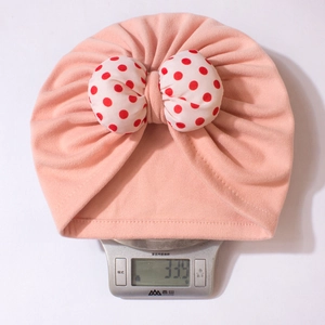Detailed weight display of pink infant knot hat with polka dot bow on electronic scale