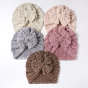 Flat lay of five soft baby beanies with oversized knit bows in a variety of warm colors