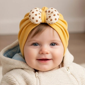 Detailed view of yellow baby turban hat with a large brown polka dot bow and soft texture