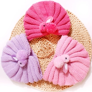 Cozy knit baby hats with cute rabbit dolls in pink and purple colors on a straw mat