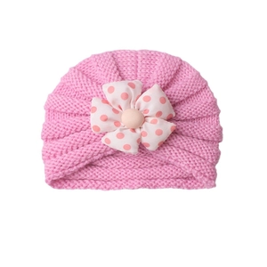 Pink knitted baby beanie with a cute polka dot flower accessory on a white background