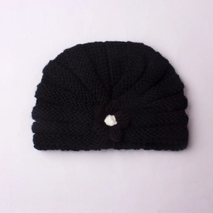 Close-up of black knitted baby hat with unique spiral texture and floral accent