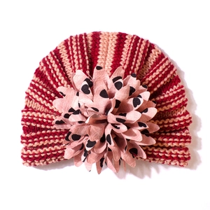 Détail d'un bonnet tricoté pour bébé à rayures rouges avec une grande fleur rose