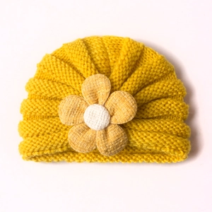 Ingwergelbe gestrickte Baby-Turban-Mütze mit großer handgefertigter Blume auf weißem Grund