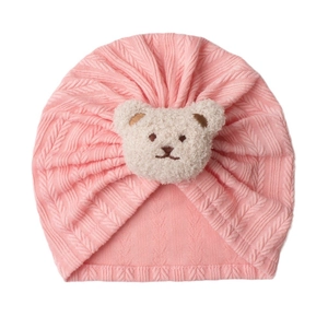 Detail der rosa gestrickten Babymütze mit Wellenstruktur und plüschigem 3D-Bärenaufnäher