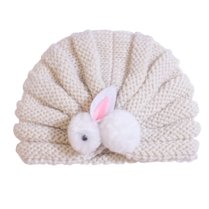 Close-up of beige knit baby turban hat with fluffy rabbit ears and soft textures