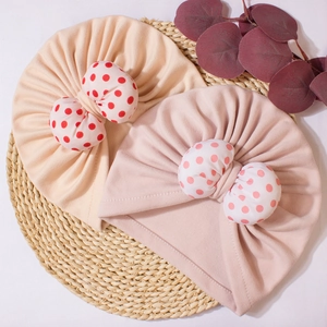 Detail of baby turban hats with red polka dot bows on soft beige and pink fabric