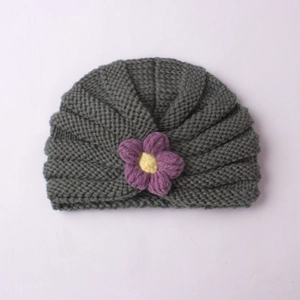 Detailed knit texture of a greyish-green baby beanie with a purple crochet flower
