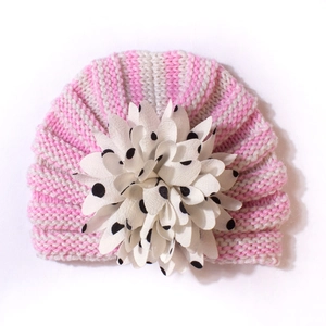 Détail du bonnet en tricot rayé rose pour bébé avec une grande fleur blanche à pois