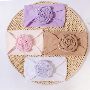 Elastic baby flower headbands in four colors displayed on a woven mat for infant hair styling