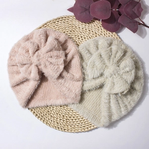 Detail of plush baby caps with large bows in soft pink and cream for winter