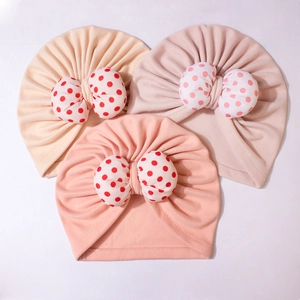 Flat lay of three soft knitted baby turbans with large polka dot bows in warm colors