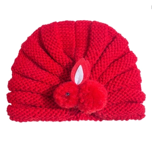 Detailed close-up of a red knitted baby turban hat with a cute 3D bunny pom-pom decoration