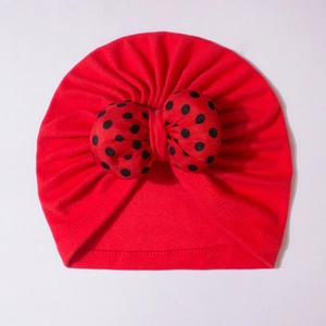 Detail of red baby turban hat with a large black polka dot bow made of soft knit cotton