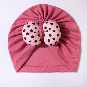 Detail of baby turban hat showing pink knit fabric and large polka dot bow embellishment