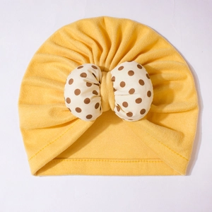 Detail of baby turban hat in bright yellow with a large beige polka dot bow on soft cotton