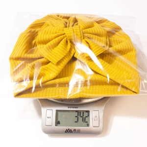 Détail du bonnet turban jaune pour bébé avec nœud pesant 34,2g sur une balance