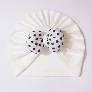 Detail of baby turban with a large black and white polka dot bow on soft white fabric