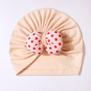 Detailed view of baby knot hat with red polka dot bow on beige soft cotton fabric