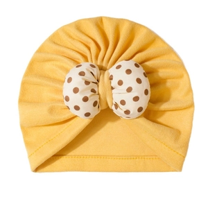 Detail of baby turban hat featuring a bright yellow knit and large polka dot bow