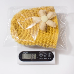 Detail showing bright yellow baby knit hat with 3D flower decoration weighing 39g