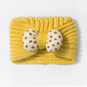 Detailed view of yellow cable knit baby headband with a beige polka dot bow accent