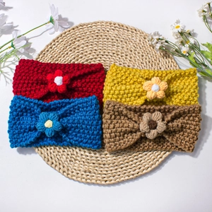 Close-up of four knitted baby headbands with crochet flowers on a woven mat