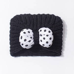 Close-up of thick black knit baby hat featuring a 3D white polka dot bow detail