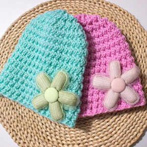 Close-up of knit baby hats in mint and pink with large floral details on straw mat