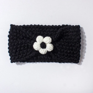 Close-up of black knitted baby headband with a white crochet flower and soft texture