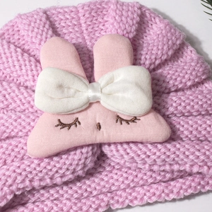 Close-up of pink knitted baby turban hat with a 3D bunny face and white bow detail