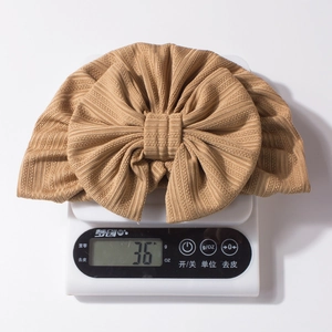 Detailed view of lightweight 36g waffle knit baby turban hat with oversized bow on scale