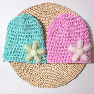 Detailed knit texture of pink and mint green baby beanies with 3D floral accents