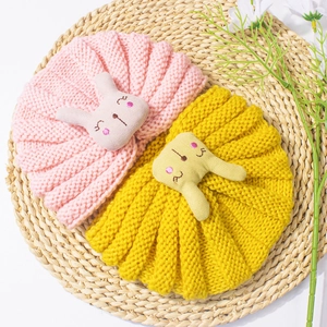 Close-up of knit baby beanies with cute rabbit ears and embroidered details on woven mat