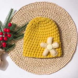 Detail of yellow handmade knit baby hat with crochet flower on natural woven mat