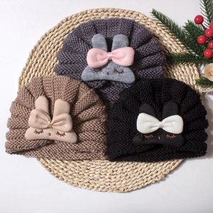 Three knit baby beanies with cute rabbit patches and bows on a woven mat