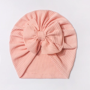 Détail de texture du turban rose pour bébé en tricot gaufré avec un grand nœud décoratif