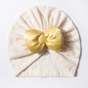 Bonnet turban bébé avec texture tricotée crème et un grand nœud en satin doré brillant