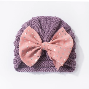 Detailed knit texture of purple baby turban hat with a large pink bow and silver stars