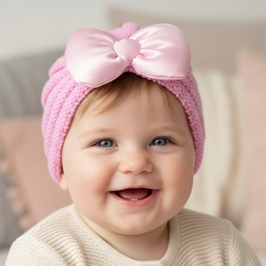 Détail du bonnet turban tricoté pour bébé avec un grand nœud en satin rose pastel